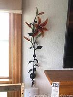 Full view of the metal and glass Tiger Lily flower wall art piece mounted on the wall next to a window and TV, showing its size and style.