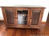 Front view of wood buffet showing carved wood doors on sides and glass door in center on hardwood floor.