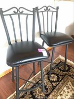 Two black metal bar stools with swiveling padded seats placed on a rug.