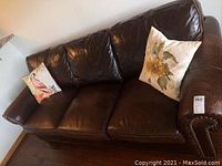 Full front view of dark brown leather Stickley Craftsman sofa with three seat cushions and two decorative throw pillows.