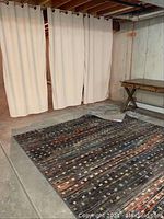 Photo of basement area showing three tan drape panels hanging and multi-colored carpet on floor.