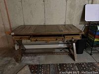 Front view of distressed wood desk with three drawers, leather-like writing surface inset, and trestle base.