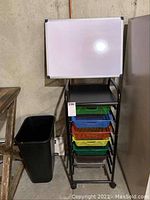 Desk area showing rolling sorter with 7 colored basket drawers, whiteboard on top, and waste bin beside it