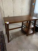Front angle view of medium brown wood office table with side shelving showing overall shape and condition.