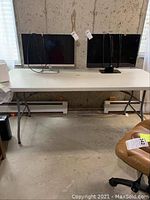 Photo of white folding table with two monitors on top, showing table length and leg structure.