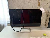 Front view of monitor showing black screen, silver bottom bezel and integrated power cable draped over the front.