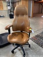 Front view of the brown leather executive desk chair on rollers showing padded seat and armrests