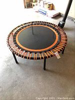 Top view of small round trampoline showing black fabric jumping surface with orange border and orange cords attached to metal frame.