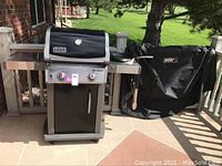 Front view of Weber Spirit propane grill with two control knobs and adjacent fitted cover on railing