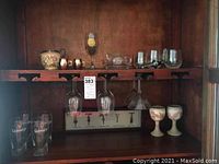 Shelf displaying mixed glassware including Guinness pint glasses, stemmed wine glasses, martini glass, stone goblets, and a glass decanter.