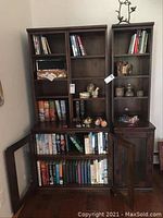 Wooden bookshelf filled with books, both hardcover and paperback, with doors open showing more books inside.