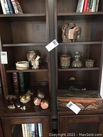 Wide view of dark wooden shelves with pottery pieces, pottery vases, ceramic bowls, mini stone chess set inside a wooden box, and wooden figurines.