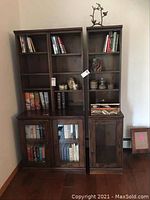 Front view of both shelving units with books and decorative items on shelves and cabinet space below with glass and wood doors.