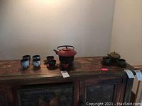 View of two Japanese tea sets on wooden cabinet, including red teapot with four cups and green teapot with matching cups and trays