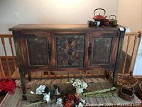 Front view of wooden sideboard with three drawers and doors showing textured and painted floral panel designs