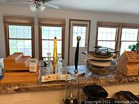 Kitchen countertop with bamboo knife block, clearly visible towel rack, glass decanters with stoppers, gray and glass bowls stacked, metal steamer basket, colander and kitchen utensils arranged.
