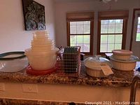 Photo of stacked clear plastic food storage containers with lids, red and green colors visible, and Corning Ware ceramic dishes with lids on counter.