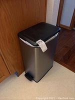Side view of stainless steel trash bin with black lid and foot pedal.