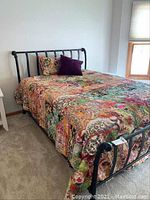Full view of queen size metal frame bed with colorful patterned bed linens and decorative pillows