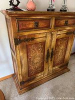 Front view of wood cabinet showing two drawers and two doors with decorative floral panels and metal hardware.