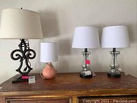 Four lamps on wooden surface showing two matching glass lamps with white shades, one metal base lamp with cream shade and small peach ceramic lamp