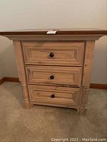 Front view of one Hickory wood bedside table showing three drawers with round black knobs and carved legs.