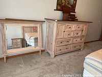 Full view of dresser with 8 drawers and 2 doors next to the matching mirror, both made of light-colored hickory wood.