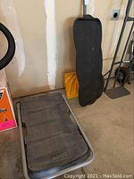 Rubbermaid dolly platform and metal frame handles leaning against wall with a black boot tray and yellow snow shovel.