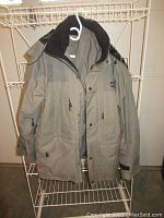 Gray Wetskins jacket hanging on rack showing front view with several zippered pockets and black collar lining.
