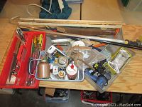 Overview photo of assorted hand tools, adhesives, measuring sticks and small hardware items organized in trays and baskets on a table.