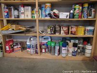 Shelf showing various spray paint cans, fuel cans, cleaning powder, oils, and boxed items for household use.
