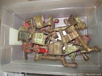 Single image showing a plastic container with nine vintage clamps, varying in paint residue and rusting.