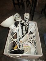Box of various vintage desk lamps seen from above showing lamp shades, cords, and clip bases.