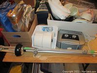 Photo of silver insulated tarp, boxed utensil holders, kitchen roll holder with two paper towel rolls, and a compact toaster on a wooden table