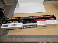 Opened collector’s box laid flat with foam trays and lightsaber hilt in plastic sleeve