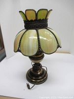 Front view of vintage decorative table lamp showing green and cream stained glass petals and metal base.