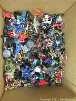 Top-down view of a box filled with many different HeroClix figurines in various poses and costumes with black bases.