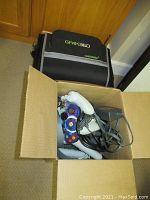Open cardboard box containing multiple Xbox 360 wired controllers, headset, power adapter and cords.
