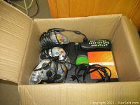Open cardboard box containing original Xbox console and accessories including three clear wired controllers, remote, power cable, and manual.