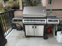Front view of stainless steel gas BBQ grill with hinged lid, four control knobs, side burner, two cabinet doors and wheels
