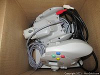 Two Sega Dreamcast wired controllers with colorful buttons inside a cardboard box, showing controller shape and cables.