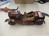 Side view of the handcrafted wooden vintage car model showing detailed elongated hood, seats, and wheels.