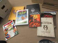 Top view of lot showing all books together on carpet, including Marvel how to draw comics, Asterix comic, Skyrim book, Oblivion and Zelda guides.