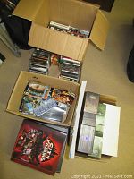 Two cardboard boxes and one open box containing stacks of PC game DVD and CD jewel cases