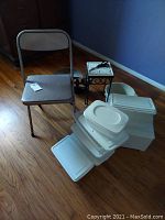 Full lot view showing folding chair, storage containers, plant stand, and bucket on hardwood floor against blue wall.