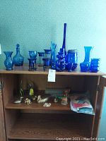 Shelf with assorted blue glass items including bottles, vases, candle holders, and metal duck figurines with animal figurines on lower shelf