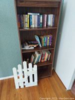 Full view of the wooden 4-shelf bookshelf filled with assorted paperback books, showing the dark wood grain finish and general condition.