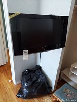 Samsung 23in TV mounted on wall with visible power cord, black frame, glossy finish.