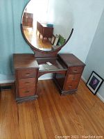 Full view of wooden vanity with glass top and attached round mirror in a room with hardwood flooring