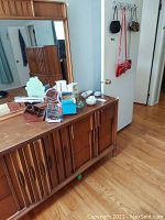 Photo showing a mid-century wooden dresser with mirror, several small glass decorative objects on its surface, two wooden jewelry cases, and purses hanging on an over-the-door metal hook on a white door.